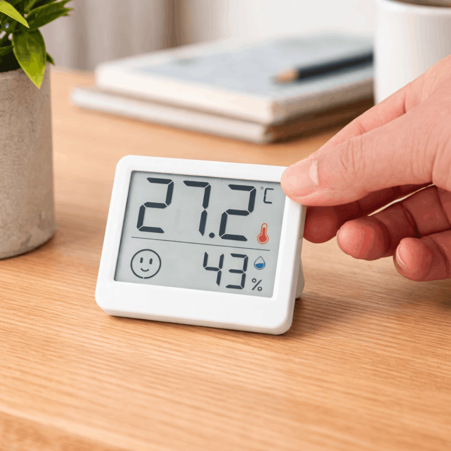 Compacte digitale hygrometer met display, toont temperatuur van 27,2 graden en luchtvochtigheid van 43 procent op een houten tafel.