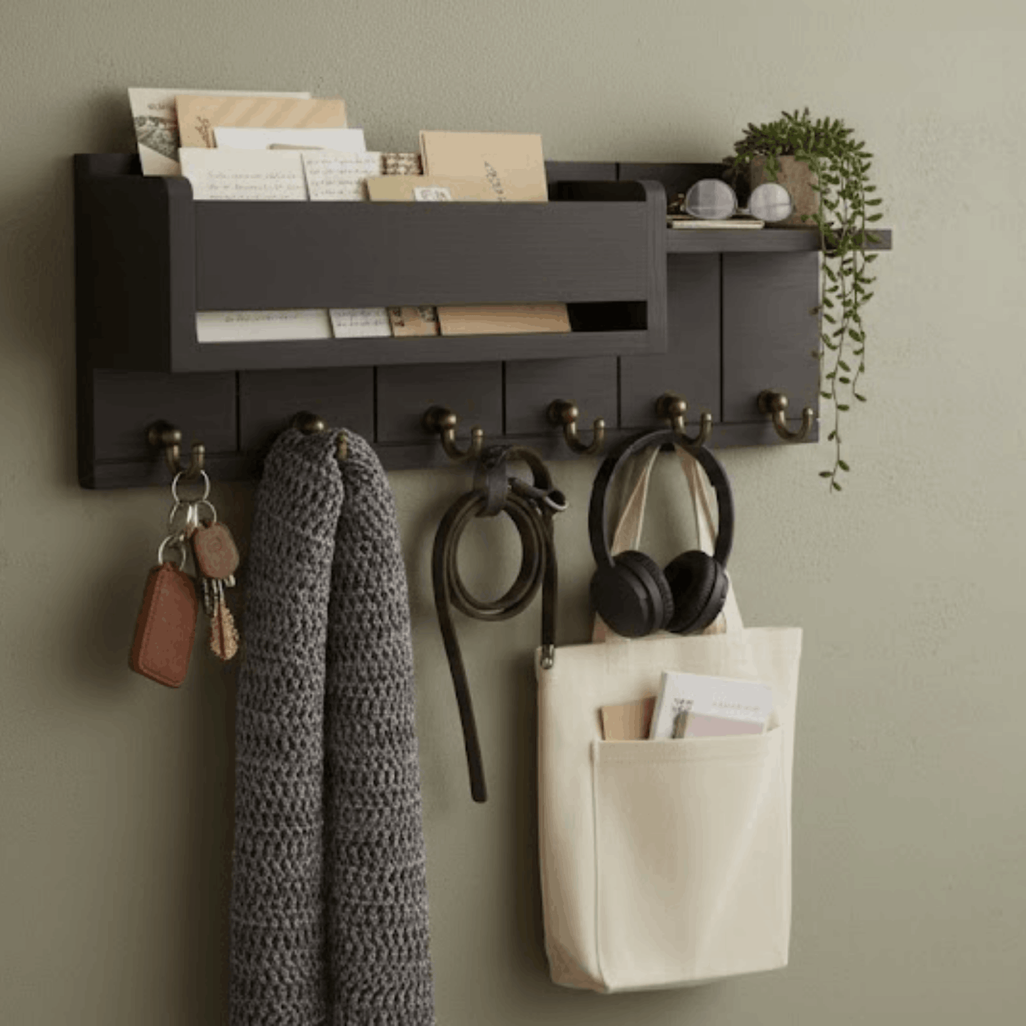 Zwart houten wandrek met sleutelhaken en brievenvak, met sjaal, koptelefoon en sleutels aan de muur.