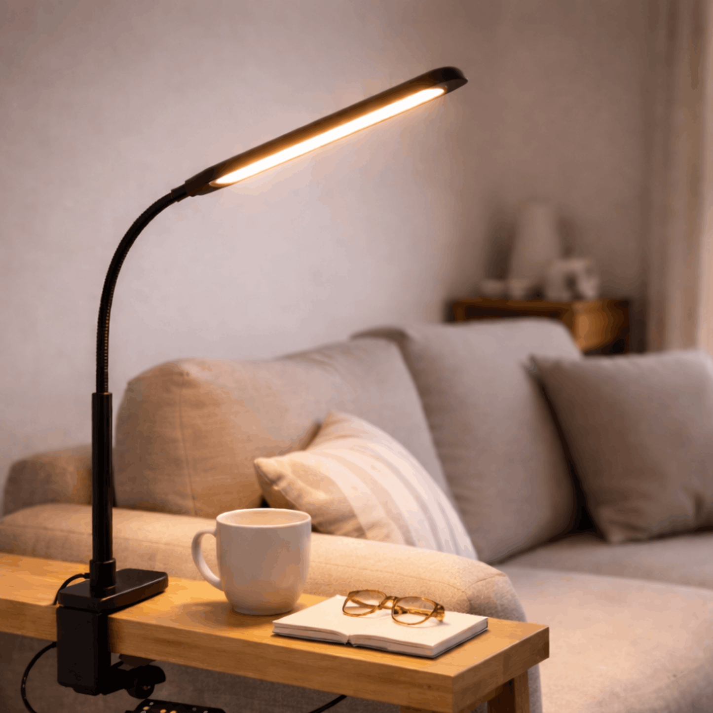 Zwarte bureaulamp met flexibele arm en smalle lichtbalk, bevestigd met klem aan een bureau naast een open boek.