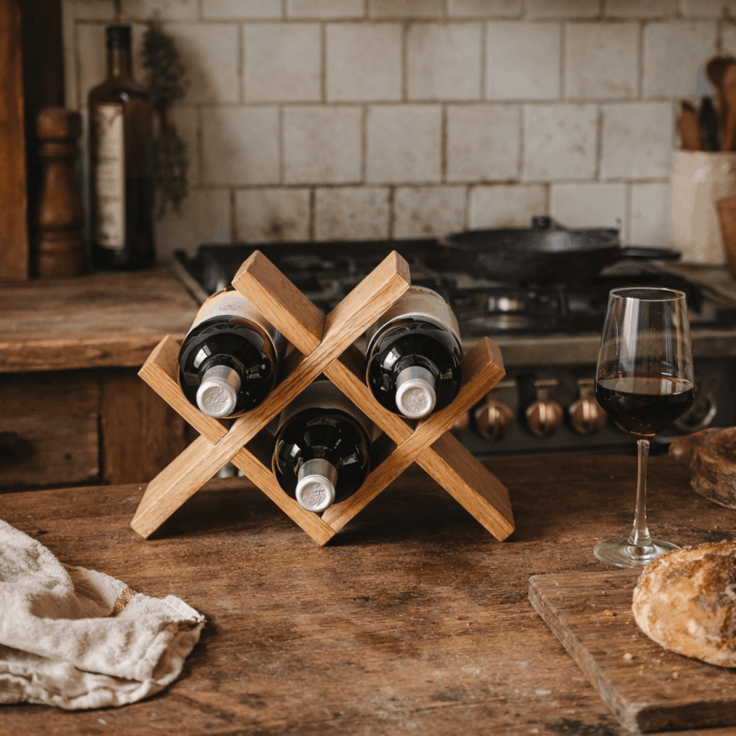 Compact houten wijnrek met kruisvormig ontwerp voor vier wijnflessen, geplaatst op een rustieke houten tafel in de keuken naast een glas rode wijn.