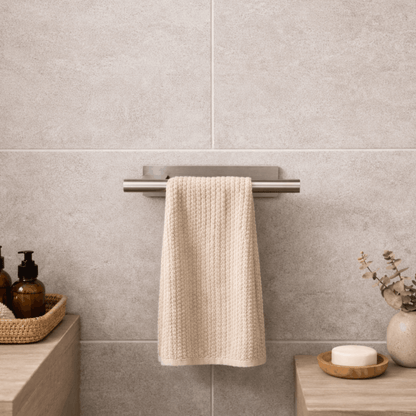 Moderne zilverkleurige handdoekhouder met handdoek, gemonteerd aan een betegelde muur in een stijlvolle badkamer naast de wastafelaccessoires.