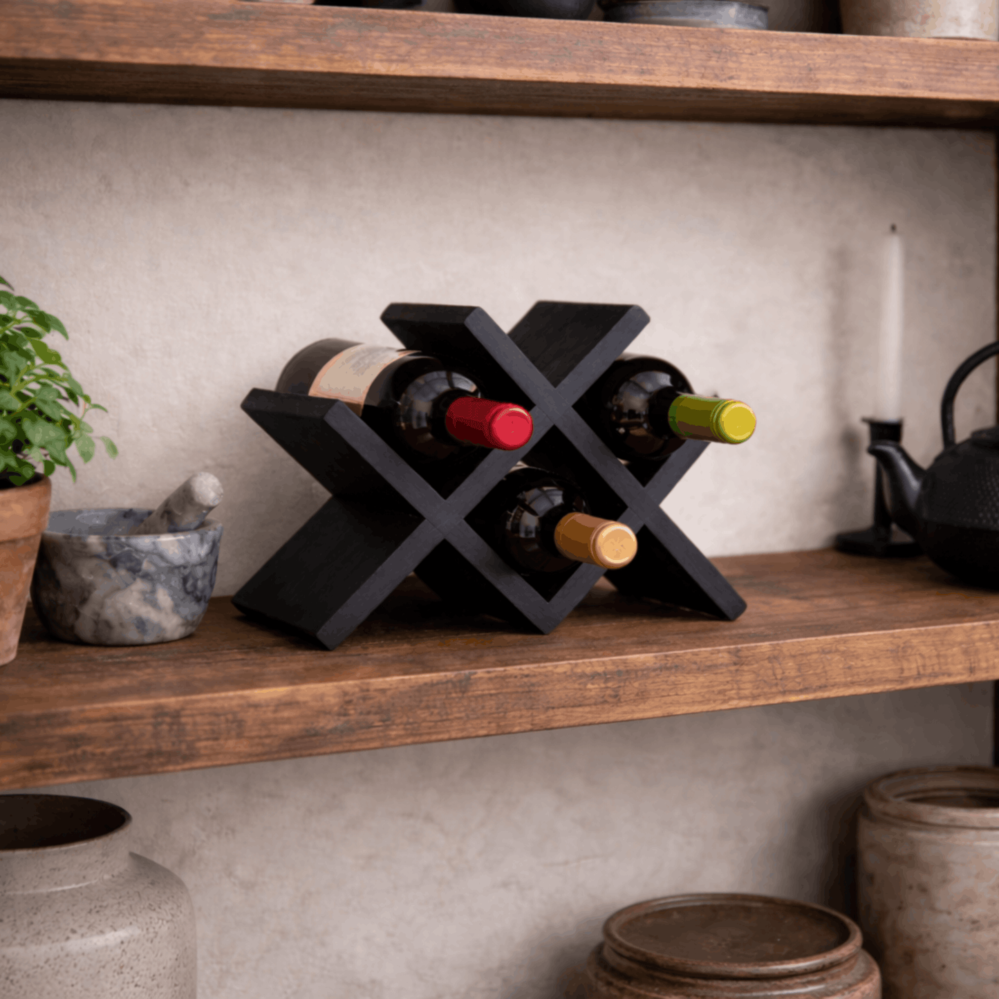 Compact zwart houten wijnrek met kruisvormig ontwerp voor vier wijnflessen, geplaatst op een houten plank in een stijlvol interieur.