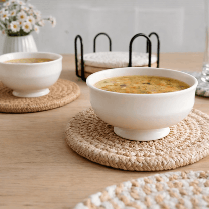 Ronde gevlochten onderzetter voor glazen met een kom soep op een houten tafel.