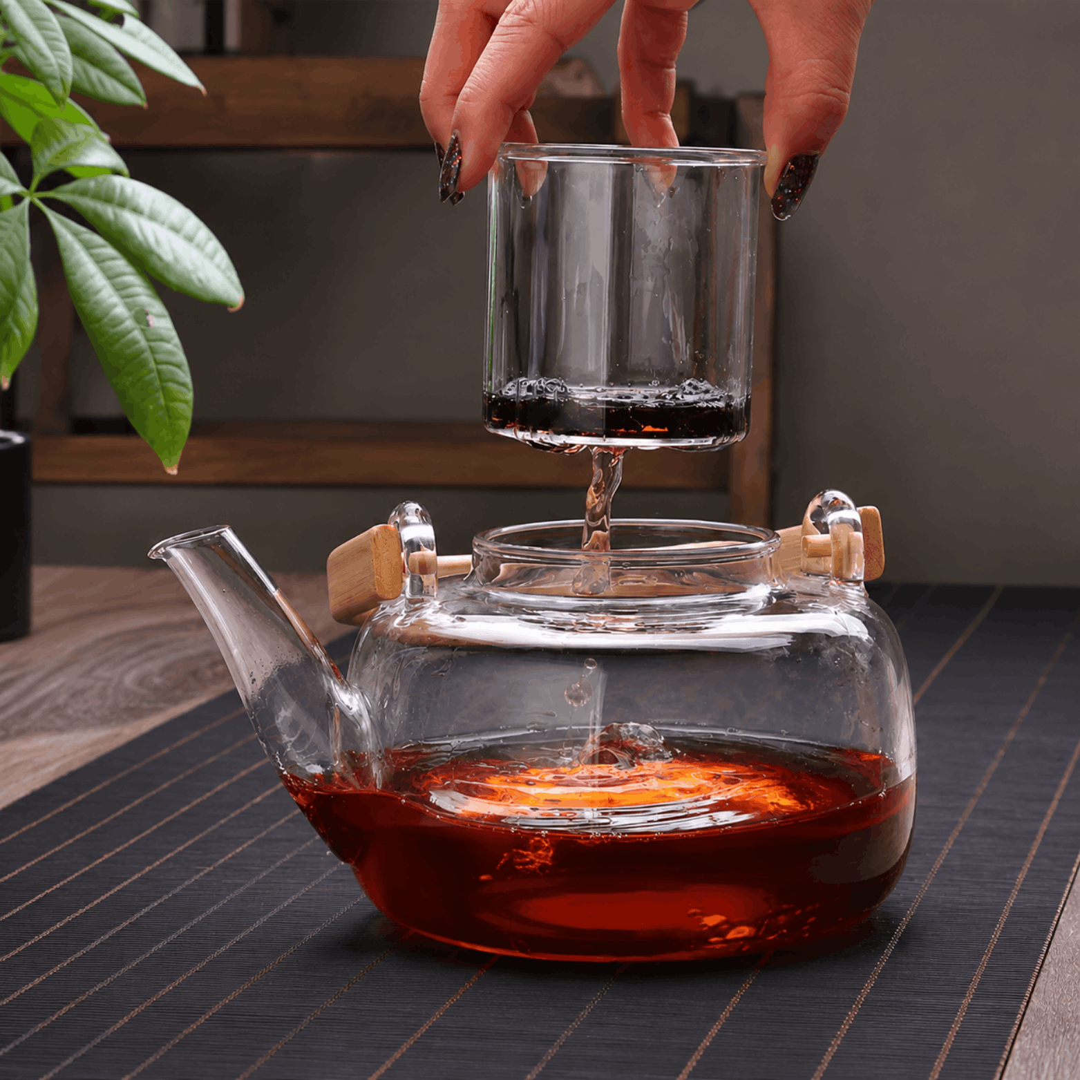 Transparante glazen theepot met thee en uitneembaar glazen filter op een houten tafel.