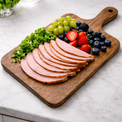 Houten snijplank met handvat gebruikt als serveerplank met gesneden vlees, druiven, aardbeien en blauwe bessen.