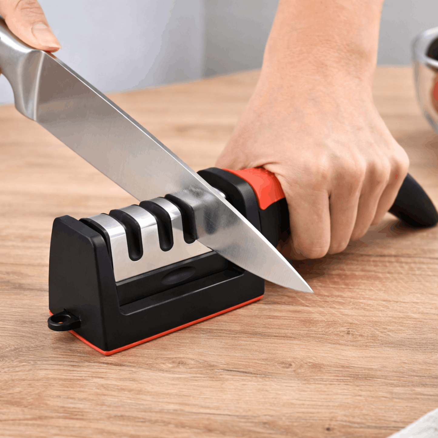 Handmatige messenslijper met meerdere slijpsleuven en stevige handgreep, gebruikt om een keukenmes te slijpen op een houten oppervlak.
