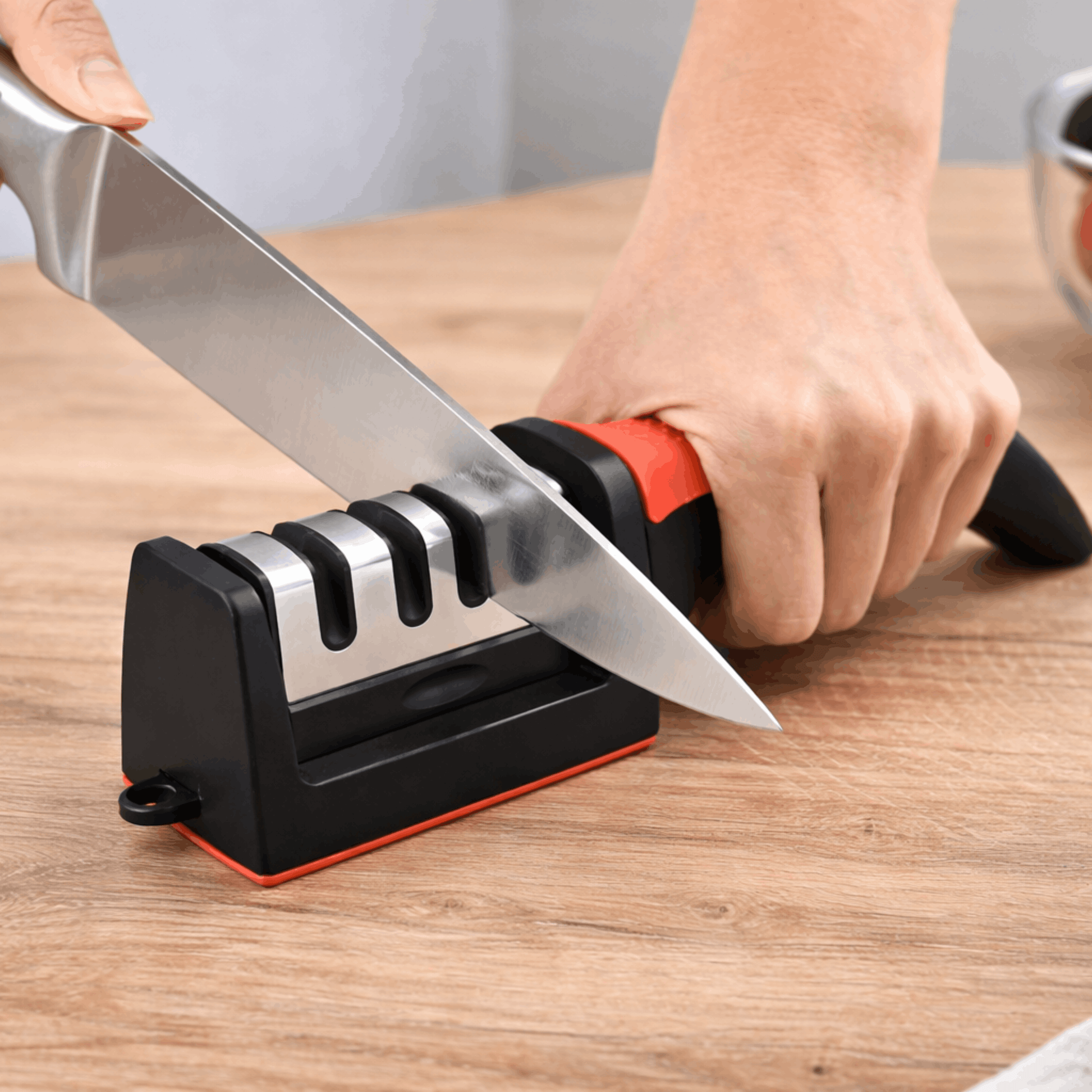 Handmatige messenslijper met meerdere slijpsleuven en stevige handgreep, gebruikt om een keukenmes te slijpen op een houten oppervlak.