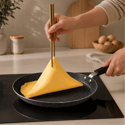 Pannenkoek wordt omgedraaid in een zwarte pannenkoekpan op een inductiekookplaat.