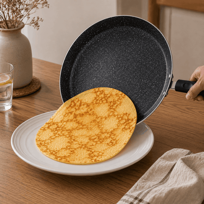 Pannenkoek wordt vanuit een zwarte pannenkoekpan op een wit bord geschoven.