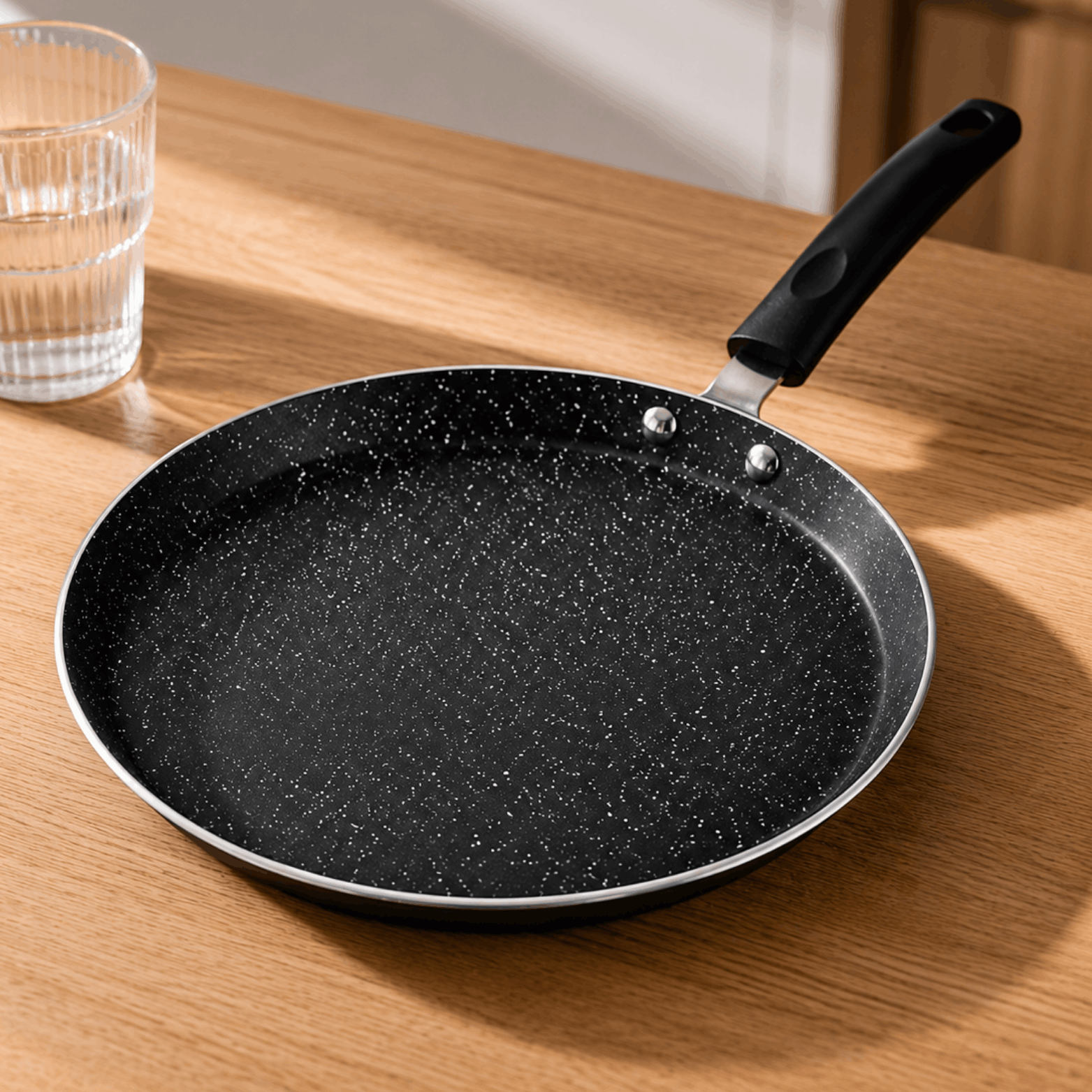Zwarte pannenkoekpan met antiaanbaklaag en handgreep op een houten tafel.