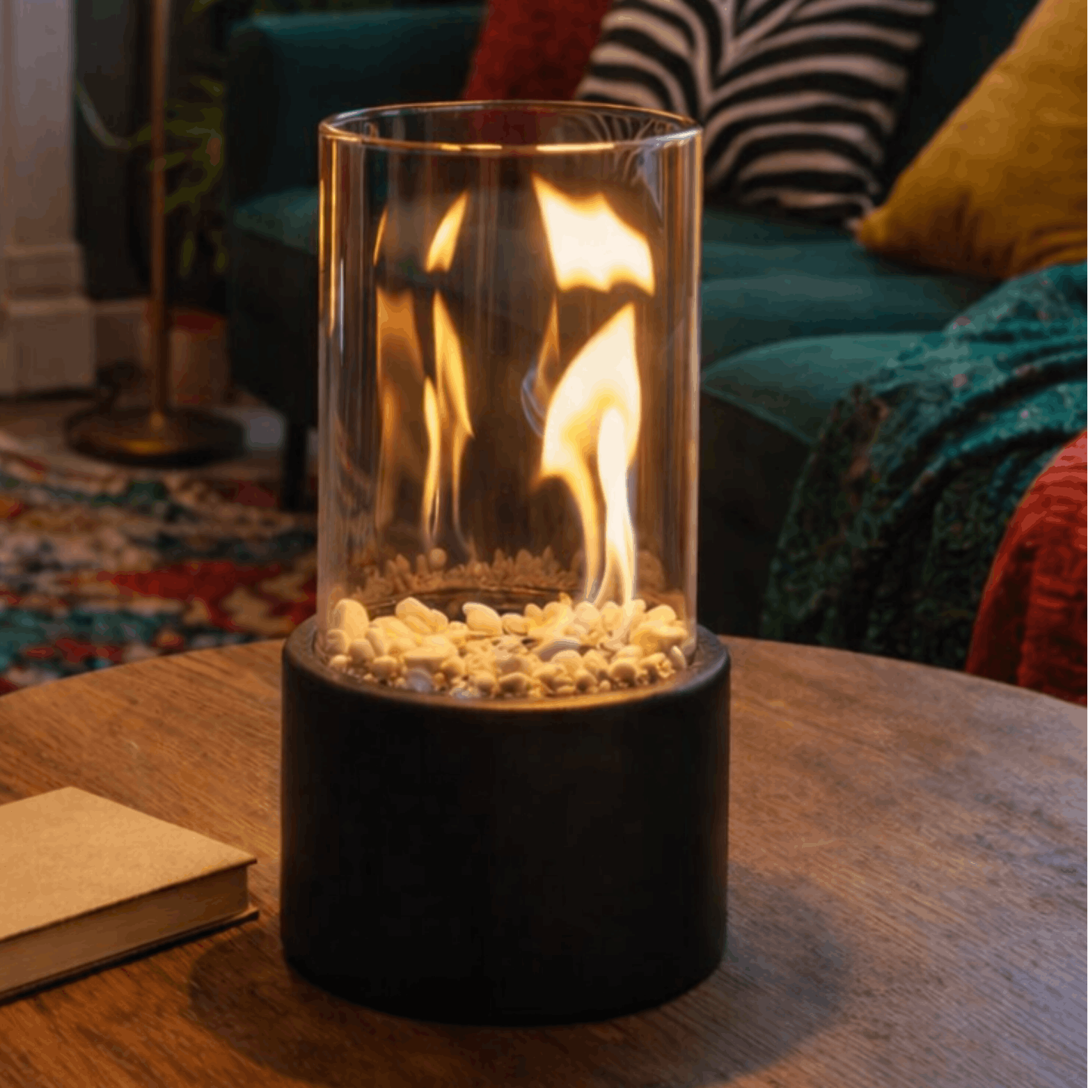 Zwarte tafelhaard met glazen cilinder en zichtbare vlammen op een houten tafel in een gezellige woonkamer.