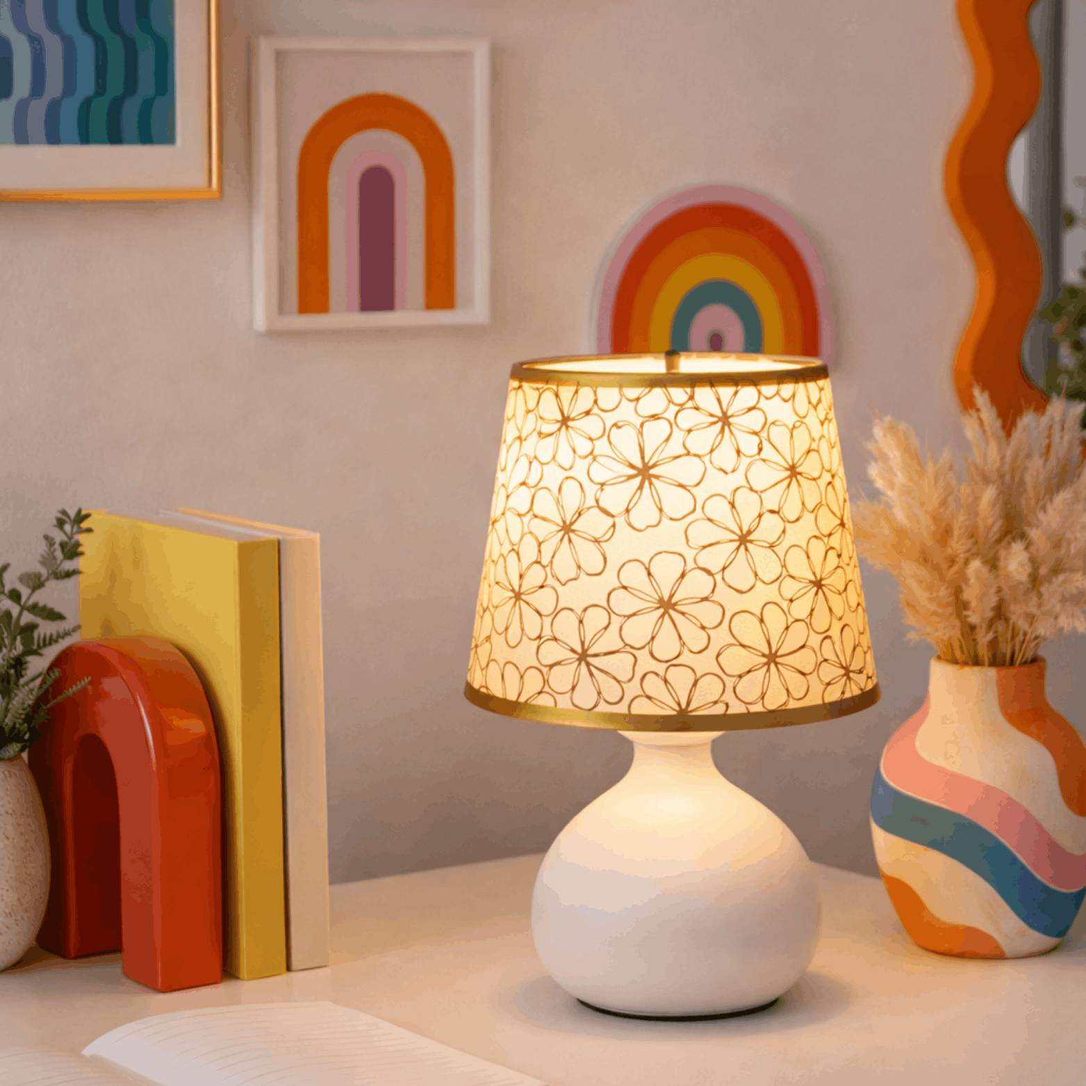 Verlichte tafellamp met bloemmotief kap op een bureau met boeken en kleurrijke decoratie.