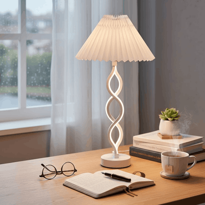 Verlichte witte tafellamp met gedraaide voet en witte plissé kap op een houten bureau.