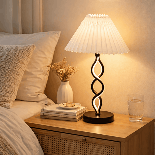 Verlichte zwarte tafellamp met gedraaide voet en witte plissé kap op een nachtkastje.