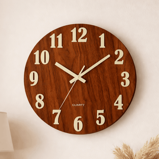 Ronde wandklok met houtlook en grote crèmekleurige cijfers, zichtbaar van voren aan een lichte muur.