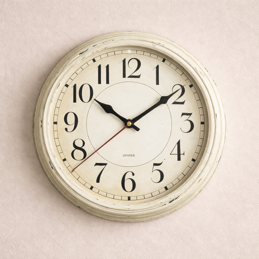 Ronde wandklok met vintage uitstraling en crèmekleurige rand, hangend aan een lichtroze muur.