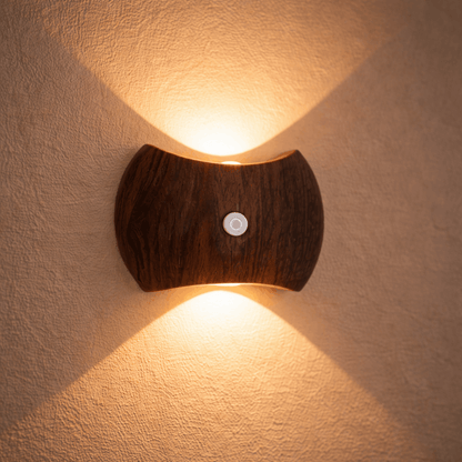 Wandlamp met donkere houten behuizing en warm licht dat omhoog en omlaag straalt op een muur.