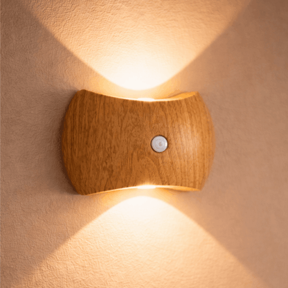 Wandlamp met lichte houten behuizing en warm licht dat omhoog en omlaag straalt op een muur.