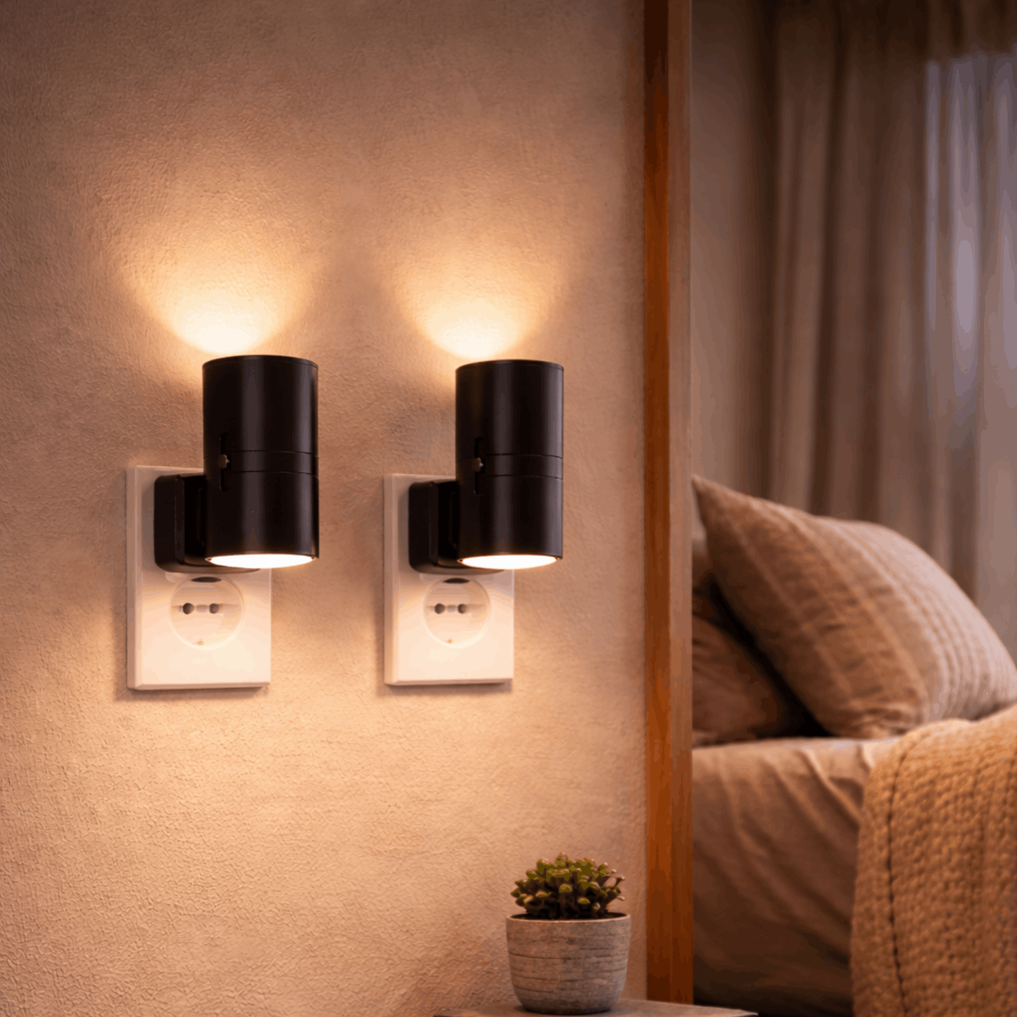 Twee moderne nachtlampjes voor in het stopcontact met warm licht, gemonteerd aan de muur naast een bed.