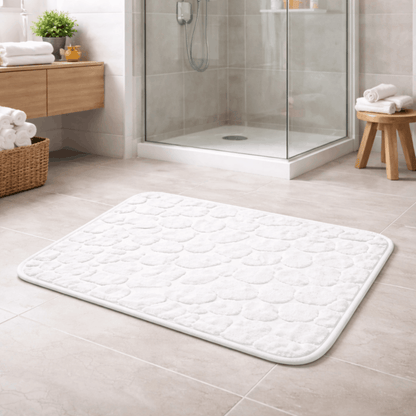 Zachte witte badmat voor de badkamer met antislip onderkant, geplaatst op een tegelvloer bij een douche.