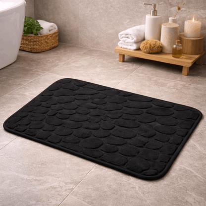 Zachte zwarte badmat met structuur en antislip onderkant, geplaatst op een tegelvloer in een moderne badkamer.