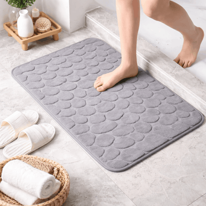 Zachte grijze badmat met steenstructuur en antislip onderkant, comfortabel om op te stappen na het douchen of baden.