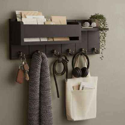 Zwart houten wandrek met sleutelhaken en brievenvak, met sjaal, koptelefoon en sleutels aan de muur.