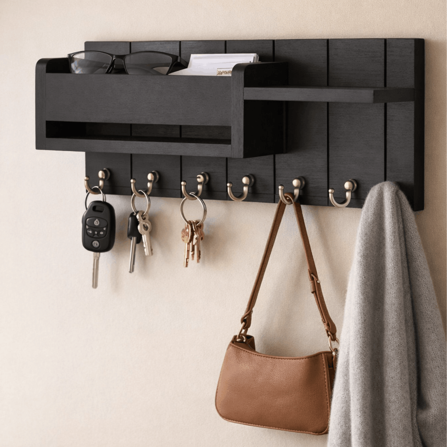 Zwart houten wandrek met sleutelhaken en opbergvak, met sleutels, tas en jas aan een lichte muur.