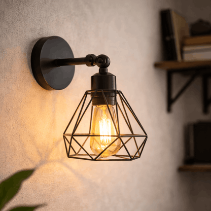 Zwarte industriële wandlamp met metalen kooi en zichtbare lichtbron, gemonteerd aan de muur voor warme sfeerverlichting.